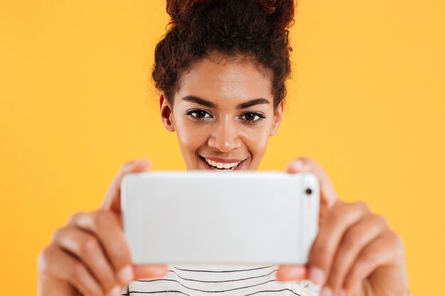 Retrato de primer plano de mujer africana sonriente haciendo fotos en el teléfono