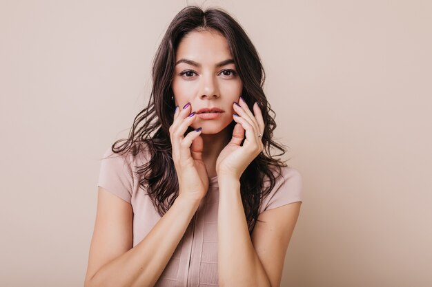 Retrato de primer plano de mujer atractiva segura con cabello oscuro ondulado. Hermosa chica en camiseta beige posando.