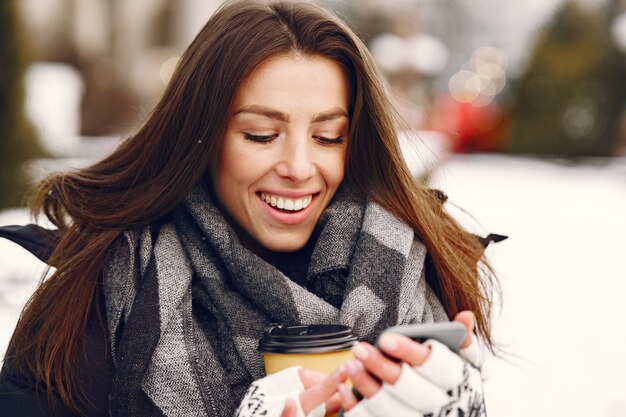 Retrato de primer plano de mujer en chaqueta negra tomando café y sosteniendo el teléfono inteligente
