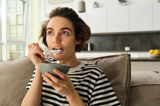 Retrato en primer plano de una mujer comiendo frente a la televisión mirando asombrada y con interés en la pantalla comiendo