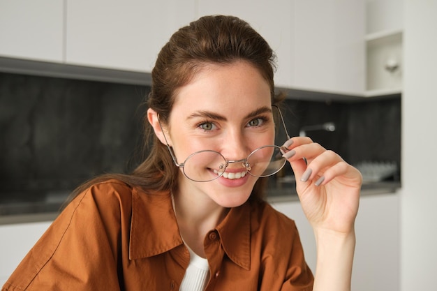 Foto gratuita retrato en primer plano de una mujer despreocupada con gafas sentada en casa en la cocina sonriendo y luciendo feliz