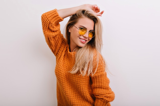 Retrato de primer plano de mujer dichosa en gafas de sol redondas de moda posando en suéter naranja nuevo