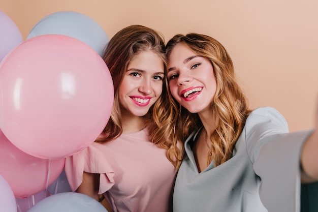 Retrato de primer plano de mujer emocionada con pelo rizado haciendo selfie con amigo