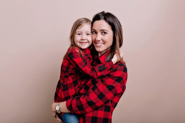 Retrato de primer plano de una mujer feliz con una niña adorable con camisetas de cuadros similares, sonríe y diviértete, hermoso retrato de familia, emociones verdaderas, pared aislada, lugar para texto