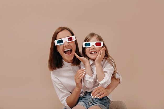 Retrato de primer plano de mujer feliz con niña viendo una película en gafas 3D con emociones sorprendidas