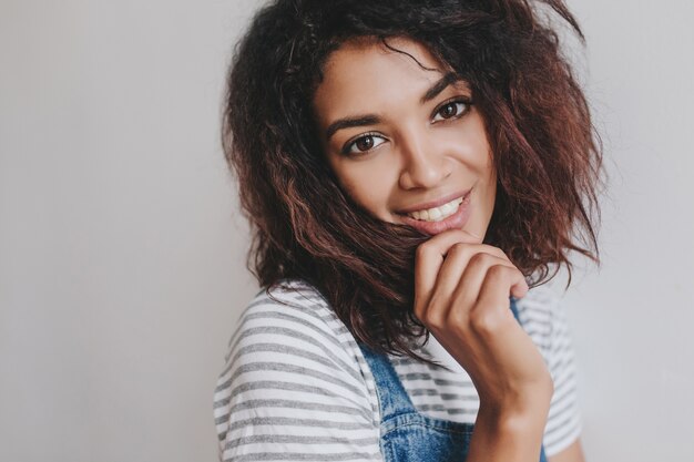 Retrato de primer plano de una mujer joven maravillosa con grandes ojos amables sonriendo suavemente en la pared de luz