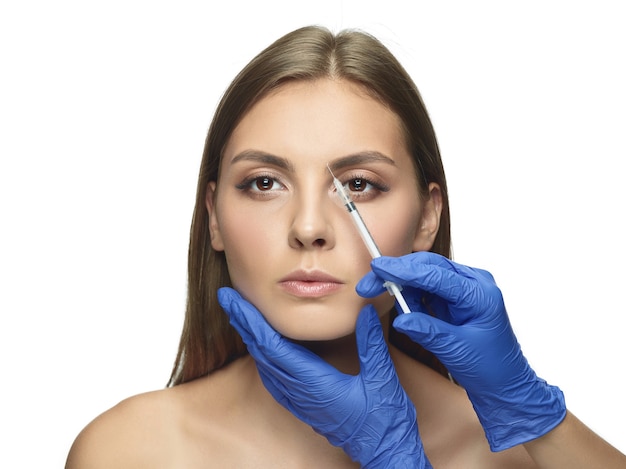 Retrato de primer plano de una mujer joven en la pared blanca. Procedimiento de cirugía de llenado. Contorno facial. Concepto de salud y belleza de la mujer, cosmetología, autocuidado, cuidado corporal y de la piel. Anti-envejecimiento.