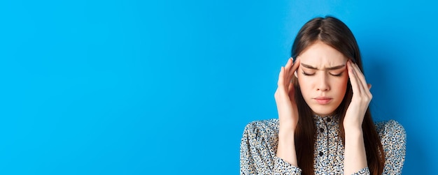 Foto gratuita retrato de primer plano de una mujer joven que se siente enferma tocando las sienes de la cabeza y frunciendo el ceño por el dolor de cabeza que tiene mi