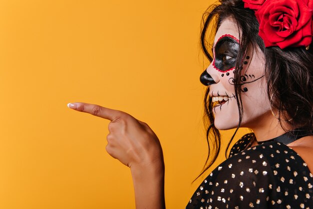 Retrato de primer plano de mujer morena latina con maquillaje de zombie. Atractiva chica de cabello oscuro en traje de muerte celebrando halloween.