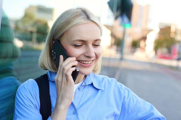 Retrato en primer plano de una mujer rubia sonriente que responde a una llamada telefónica hablando por teléfono de pie