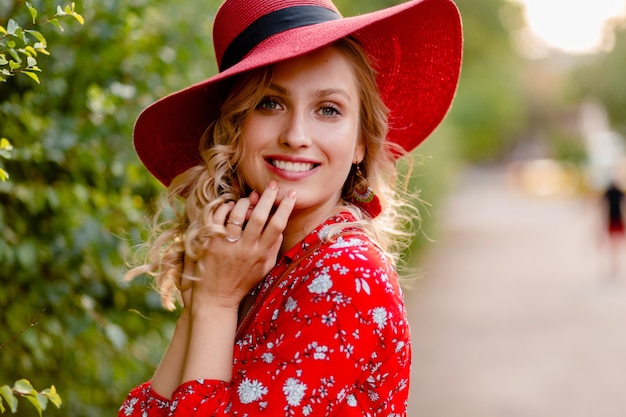 Retrato de primer plano de mujer sonriente rubia elegante atractiva en traje de moda de verano de sombrero rojo de paja y blusa con estilo de pelo rizado de sonrisa