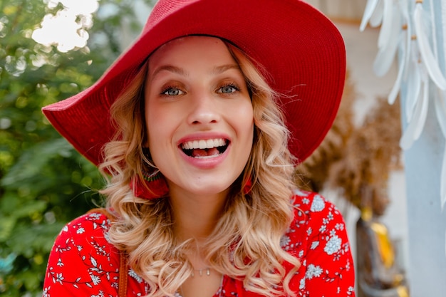 Retrato de primer plano de mujer sonriente rubia con estilo atractivo en traje de moda de verano de blusa y sombrero rojo de paja con sonrisa