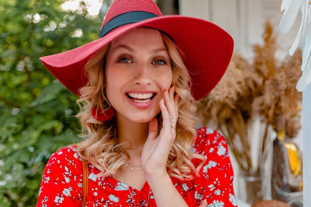 Retrato de primer plano de mujer sonriente rubia con estilo atractivo en traje de moda de verano de blusa y sombrero rojo de paja con sonrisa