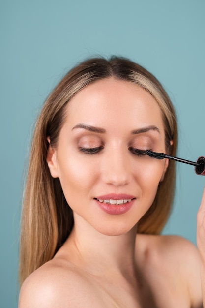 Retrato de primer plano de mujer en topless con piel perfecta y maquillaje natural, labios desnudos, sosteniendo varita de rímel