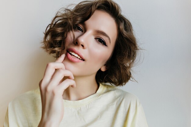 Retrato de primer plano de niña blanca pensativa con sonrisa suave. Foto de hermosa dama caucásica con peinado corto aislado en la pared de luz.