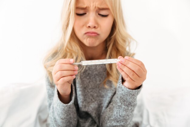 Retrato de primer plano de niña infeliz enferma con termómetro