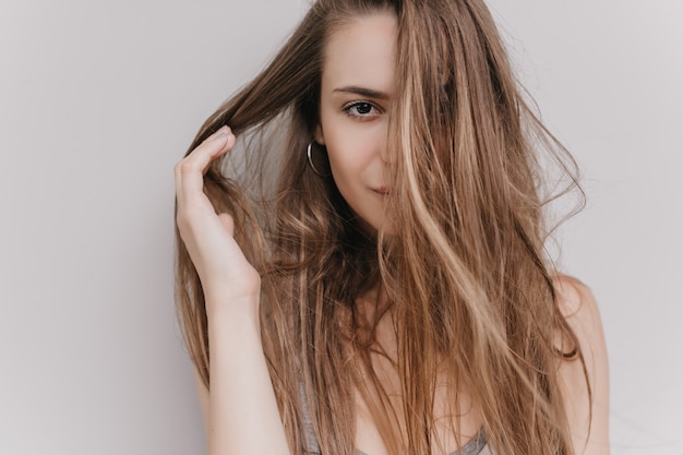 Retrato de primer plano de niña de ojos oscuros aislada. Filmación en interiores de encantadora dama europea jugando con cabello castaño.