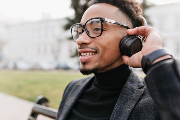 Retrato de primer plano de niño mulato despreocupado aislado. Foto al aire libre de escalofriante modelo masculino morena con piel morena posando en auriculares.