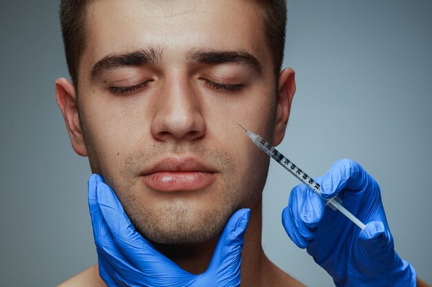 Retrato de primer plano de perfil de joven aislado en estudio gris, procedimiento de cirugía de llenado