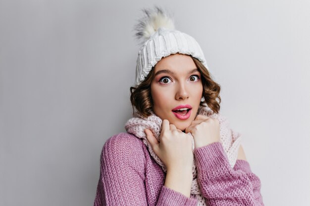 Retrato de primer plano de una romántica mujer pálida con lindo gorro de punto aislado en la pared púrpura. Bonita chica de ojos marrones en pañuelo blanco posando