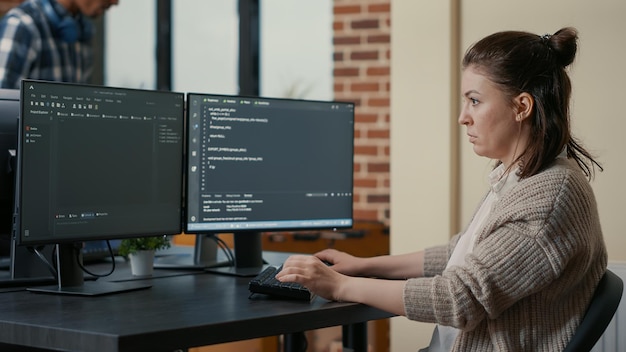 Retrato de programador enfocado escribiendo código mirando múltiples pantallas de computadora mostrando algoritmo de lenguaje de programación. Desarrollador de software codificando mientras sus colegas trabajan en equipo en segundo plano.