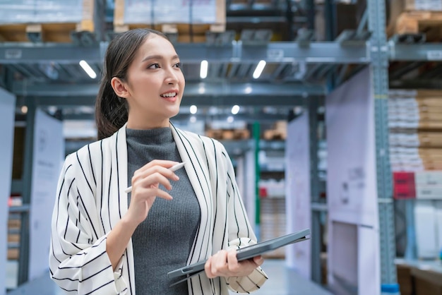 Retrato de la propietaria de una empresa asiática que usa una tableta digital para verificar la cantidad de inventario de productos en stock en el estante del almacén de distribución, el servicio de envío y entrega comercial de fábrica logística