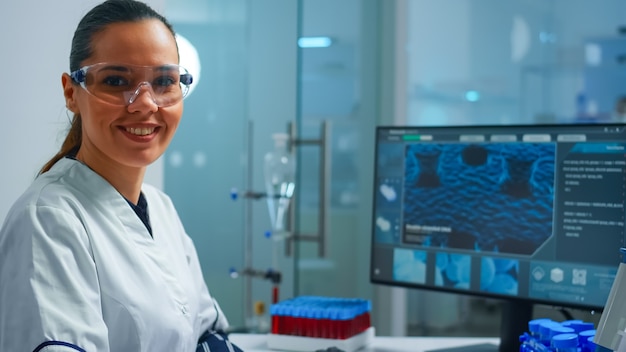 Retrato de un químico sonriente con gafas de seguridad en el laboratorio mirando a la cámara. Equipo de médicos científicos que examinan la evolución del virus utilizando herramientas de alta tecnología y química para la investigación científica, vacuna