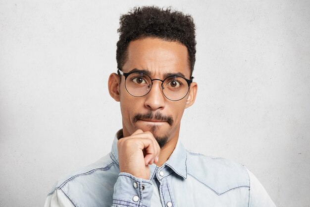 Retrato de raza mixta hombre barbudo centrado serio con peinado afro, mantiene la mano en la barbilla, presiona los labios