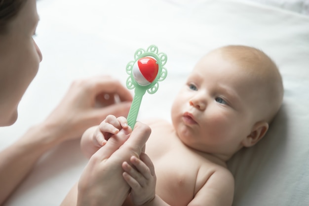 Retrato de un recién nacido lindo mirando la mano de la madre con un sonajero