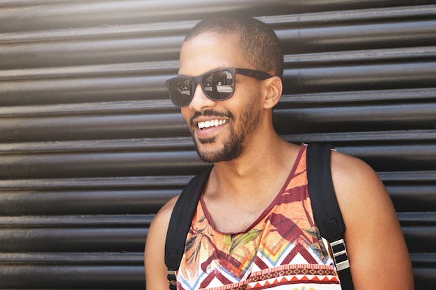 Retrato recortado de sonriente guapo hombre afroamericano con gafas de sol de pie contra la pared negra