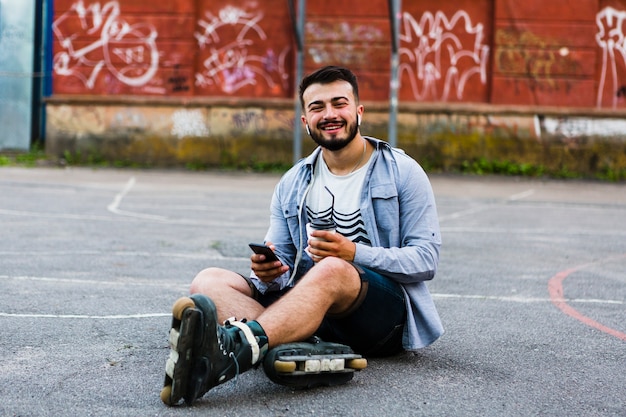Retrato de un rollerskater masculino joven con teléfono celular y taza de disposición
