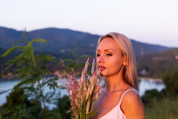 Retrato romántico de joven mujer caucásica en vestido de verano disfrutando de relajarse en el parque en la montaña con increíbles vistas al mar tropical