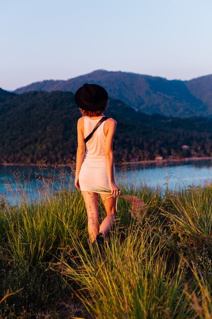 Foto gratuita retrato romántico de joven mujer caucásica en vestido de verano disfrutando de relajarse en el parque en la montaña con increíbles vistas al mar tropical