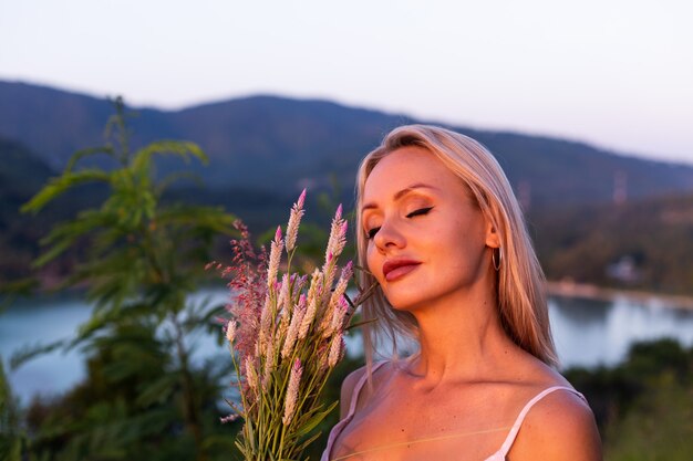 Retrato romántico de joven mujer caucásica en vestido de verano disfrutando de relajarse en el parque en la montaña con increíbles vistas al mar tropical