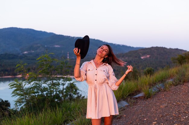 Retrato romántico de joven mujer caucásica en vestido de verano disfrutando de relajarse en el parque en la montaña con increíbles vistas al mar tropical