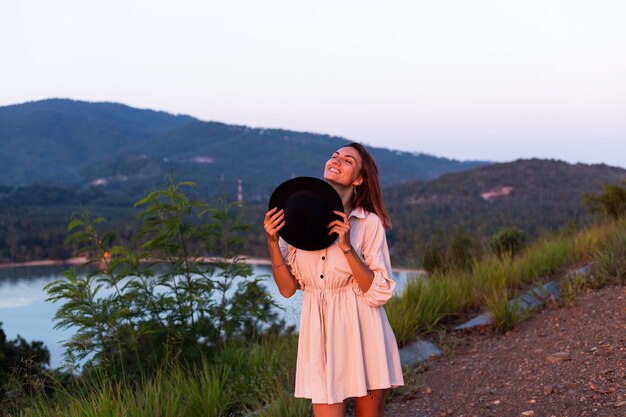 Retrato romántico de joven mujer caucásica en vestido de verano disfrutando de relajarse en el parque en la montaña con increíbles vistas al mar tropical