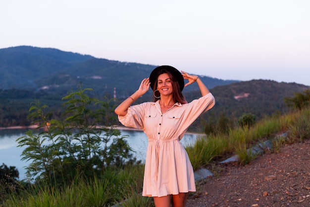 Retrato romántico de joven mujer caucásica en vestido de verano disfrutando de relajarse en el parque en la montaña con increíbles vistas al mar tropical