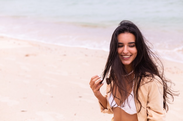 Retrato romántico de mujer en la playa en día ventoso, luz cálida del atardecer.