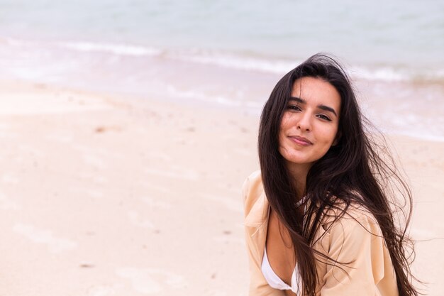 Retrato romántico de mujer en la playa en día ventoso, luz cálida del atardecer.