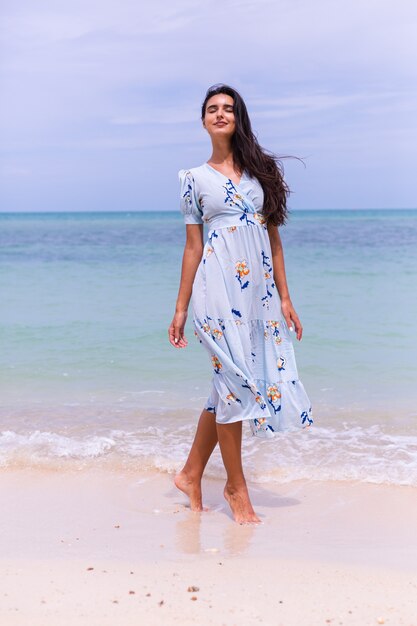 Retrato romántico de mujer con vestido largo azul en la playa por el mar en día ventoso