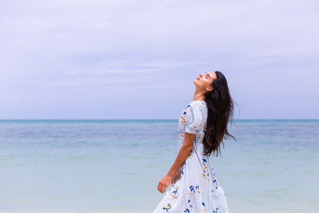 Retrato romántico de mujer con vestido largo azul en la playa por el mar en día ventoso