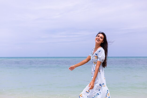 Retrato romántico de mujer con vestido largo azul en la playa por el mar en día ventoso