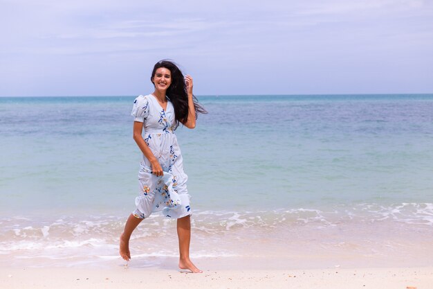 Retrato romántico de mujer con vestido largo azul en la playa por el mar en día ventoso