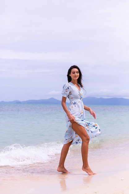 Retrato romántico de mujer con vestido largo azul en la playa por el mar en día ventoso