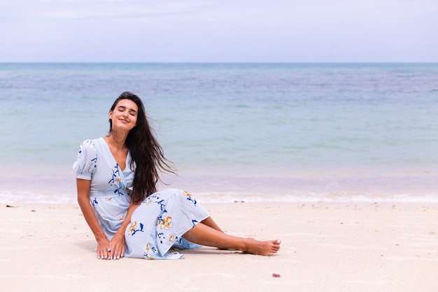 Retrato romántico de mujer con vestido largo azul en la playa por el mar en día ventoso