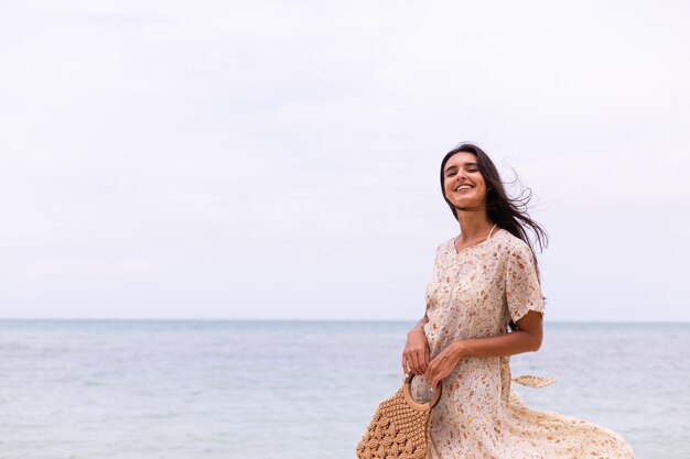 Retrato romántico de mujer con vestido largo en la playa en día nublado con viento.