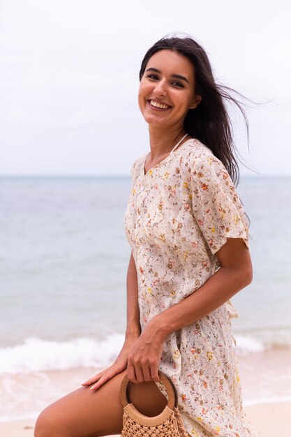 Retrato romántico de mujer con vestido largo en la playa en día nublado con viento.