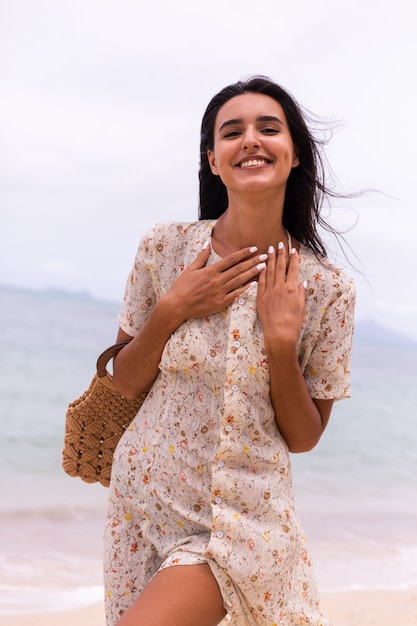 Retrato romántico de mujer con vestido largo en la playa en día nublado con viento.