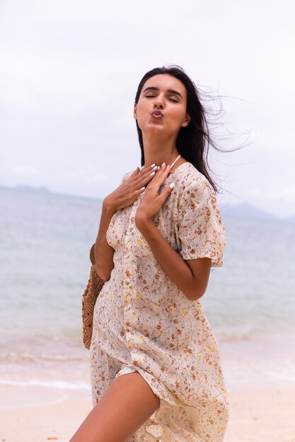 Retrato romántico de mujer con vestido largo en la playa en día nublado con viento.