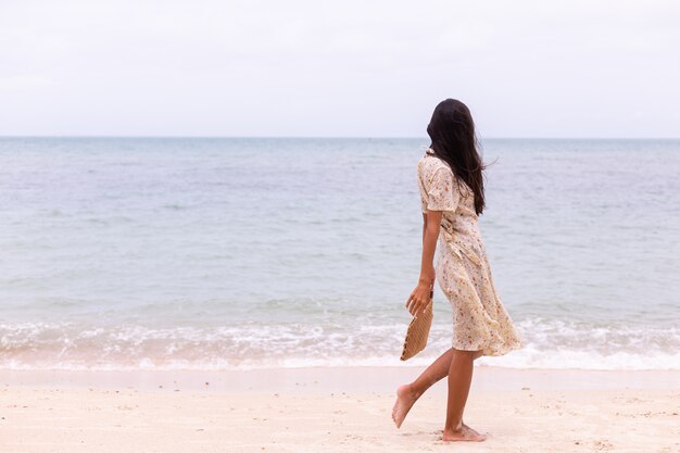 Retrato romántico de mujer con vestido largo en la playa en día nublado con viento.